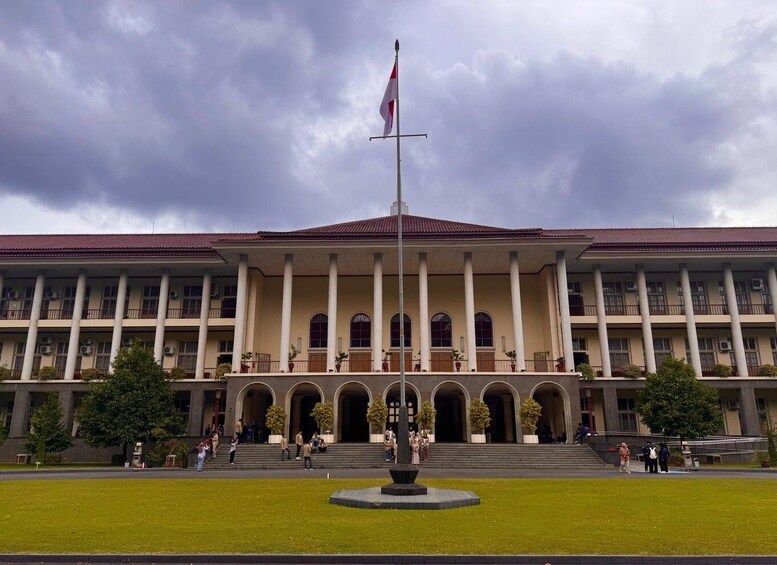 A large institutional building with a central flagpole, arched windows, and a symmetrical facade. 1