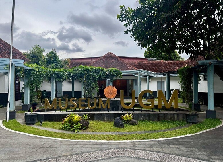 A museum entrance with a large sign, greenery, and traditional architecture. 3