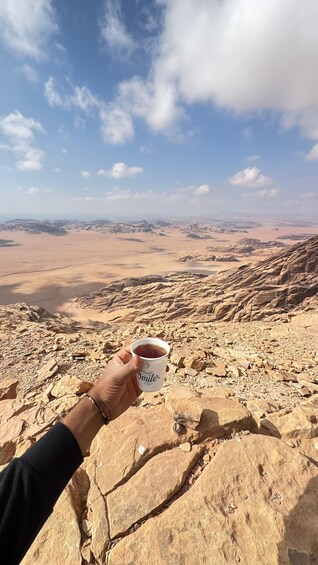 A hand holding a mug with 'Happy World Smile Day' text, overlooking a rocky desert landscape with distant mountains. 4