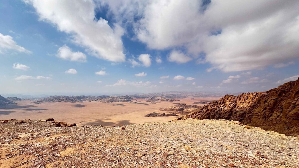 A rocky desert landscape with a view of distant mountains under a partly cloudy sky. 1
