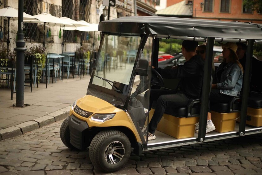 A yellow golf cart with passengers, parked on a cobblestone street with outdoor seating. 2