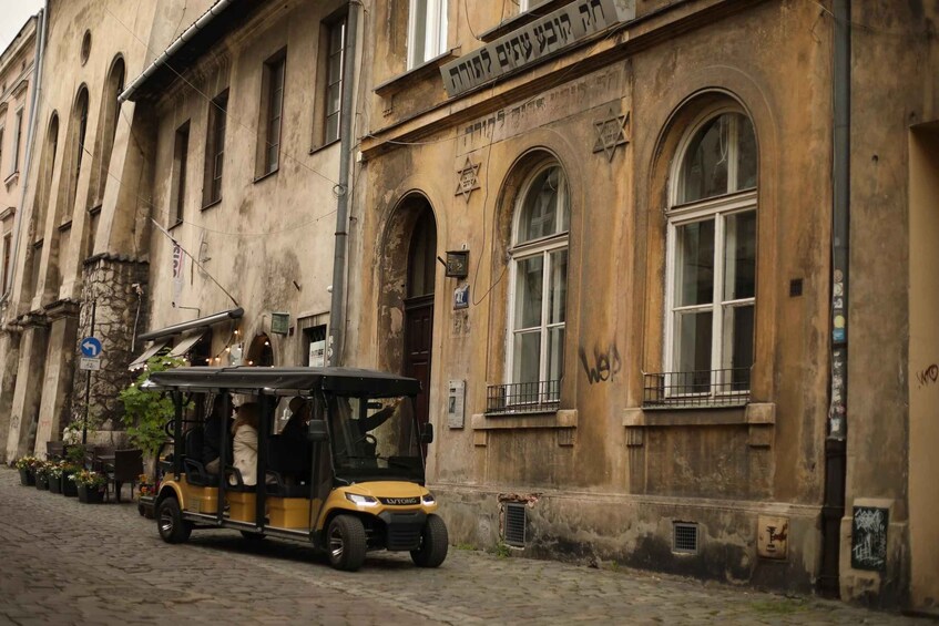 A yellow trolley parked on a cobblestone street in front of a historic building with arched windows and Hebrew signage. 5