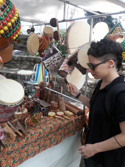 A person arranging colorful drums and musical instruments at an outdoor market. 1