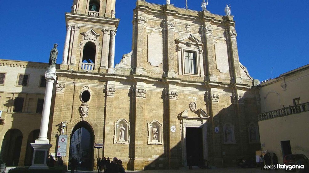 A historic church with a bell tower and statues, surrounded by a square with people. 5