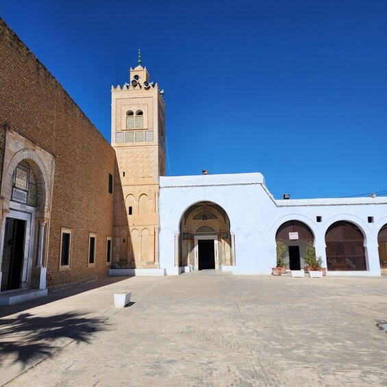 A courtyard with a tall tower, a white building with arches, and a brick building. 5