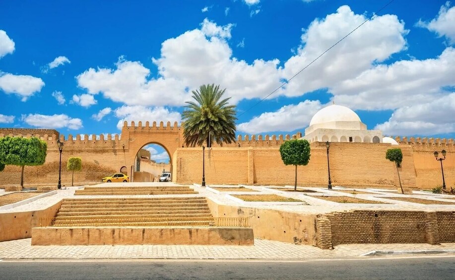 A historical fort with a large archway, palm trees, and a dome structure. 2