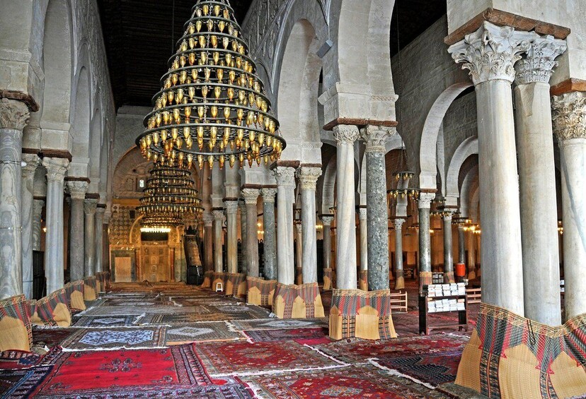 An interior with a large, ornate chandelier, columns, and patterned rugs. 4