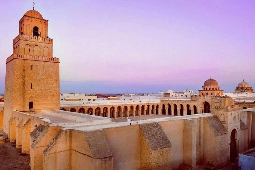 A historic cityscape with a prominent tower, domed structures, and a series of arches. 1