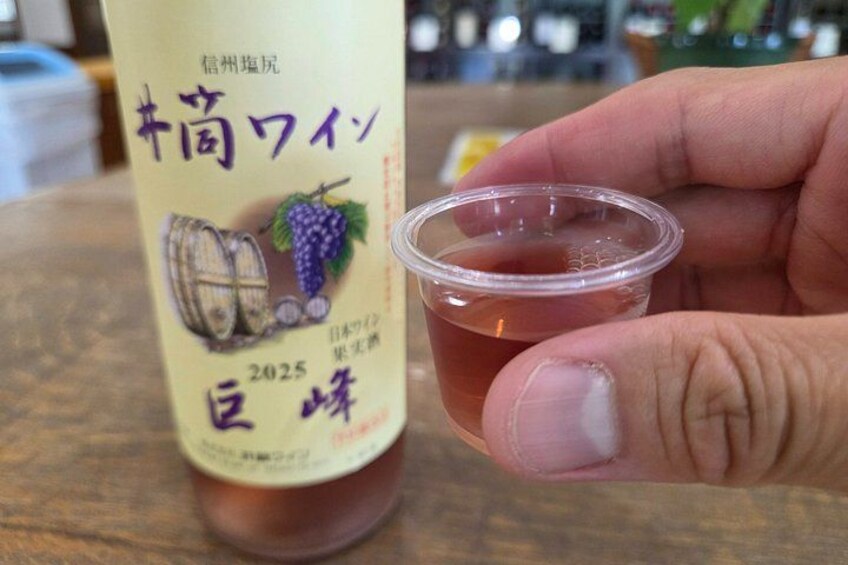 A hand holding a small plastic cup with a beverage next to a bottle with Japanese text and a barrel illustration. 2