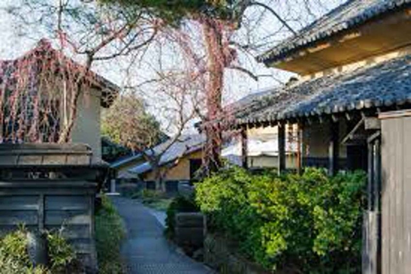 A traditional Japanese street with wooden buildings, a stone pathway, and lush greenery. 1