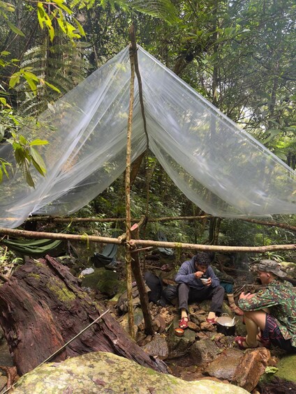 A makeshift shelter in a forest, with people sitting and eating. 2