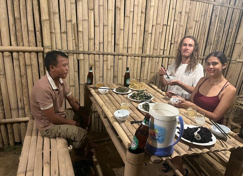 A group of people dining at a wooden table in a rustic setting with bamboo walls. 3