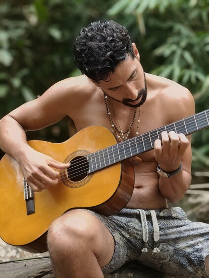 A shirtless man playing an acoustic guitar outdoors. 4