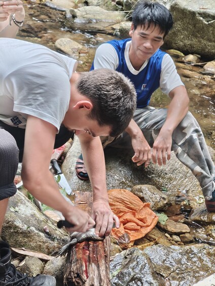 Two individuals engaged in an outdoor activity, possibly involving a natural resource, with a stream and rocks in the background. 2
