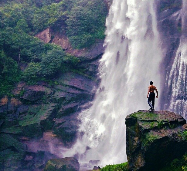 A waterfall cascading down a rocky cliff with a person standing on a ledge. 1