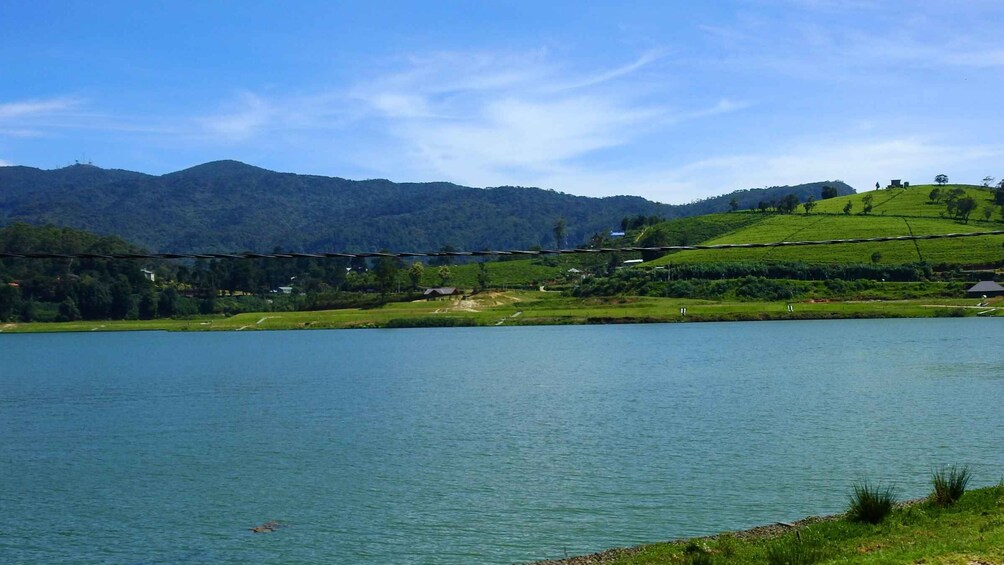 A calm lake surrounded by green hills and a clear blue sky. 2
