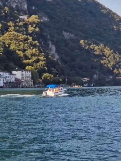 A boat on a calm lake with buildings and a forested hill in the background. 2
