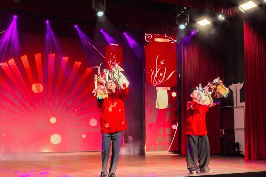 Two individuals on a stage with red curtains and a fan-shaped light display. 2