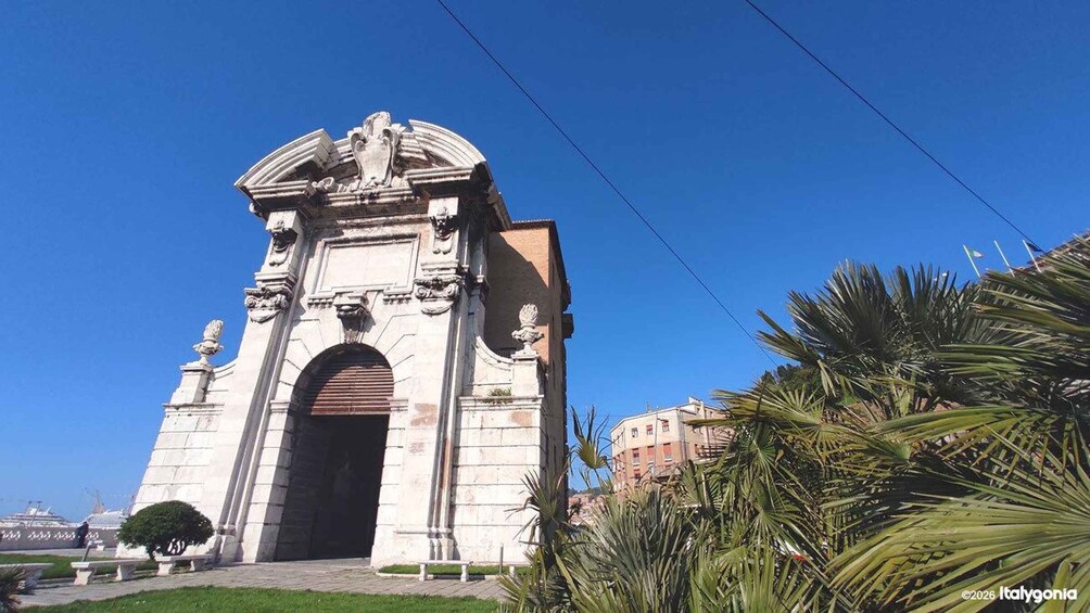 A historic stone archway with intricate carvings and a dome on top, surrounded by palm trees and a clear blue sky. 2