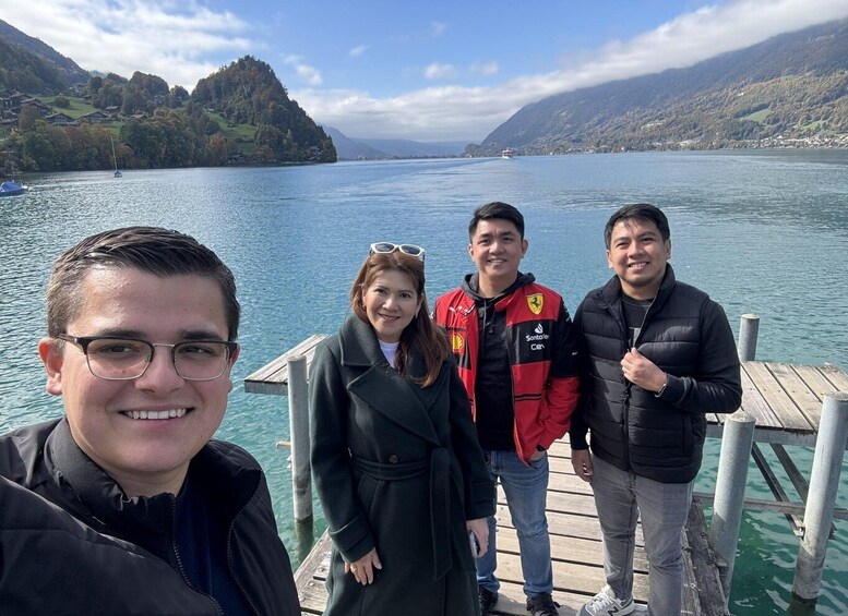 A group of people on a wooden dock by a lake with mountains in the background. 4