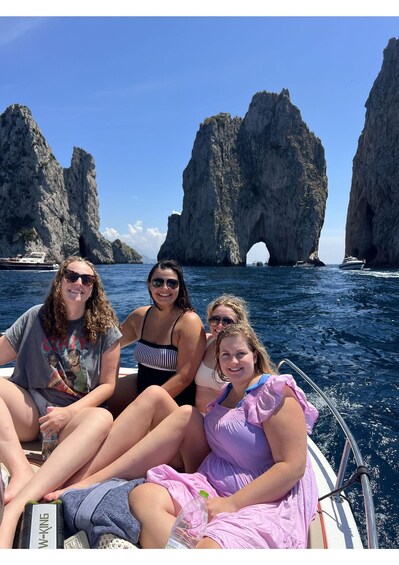 Four people on a boat with a rocky coastline in the background. 4