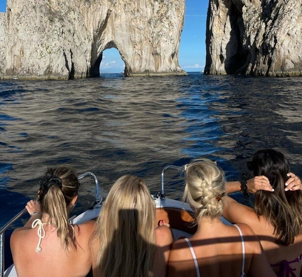 A boat with passengers facing a large rock formation with a natural arch. 2