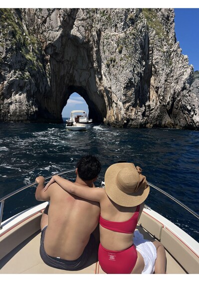 A boat with two people, a man and a woman, looking at a large rock formation with a natural arch. 5