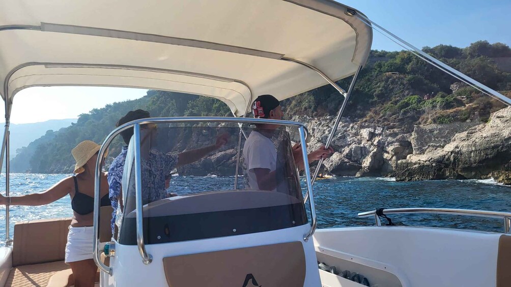 A boat with a canopy, rocky coastline, and clear blue water. 3