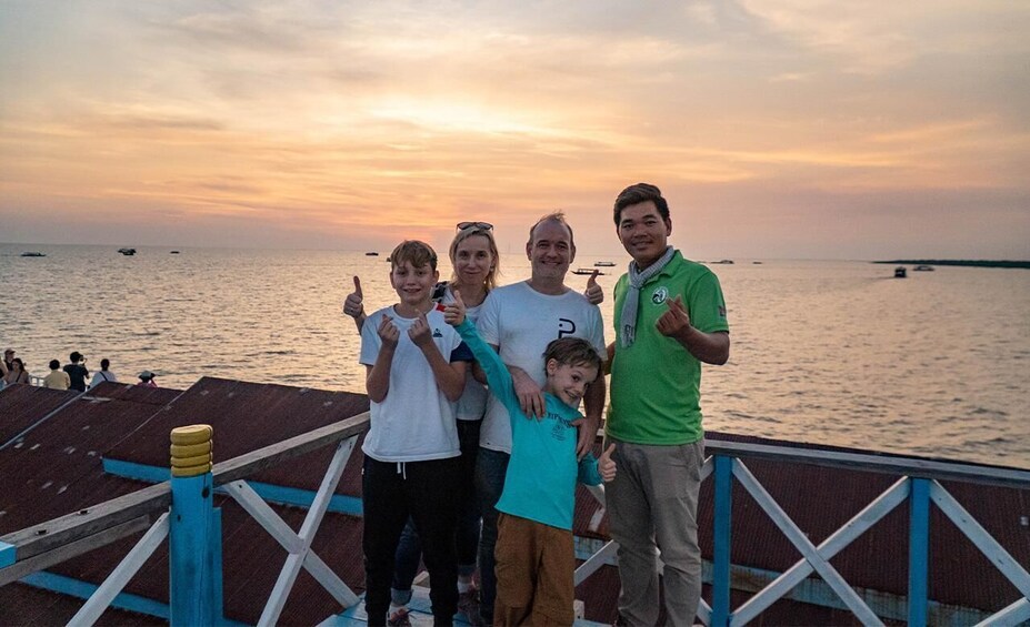 A group of people on a dock with a sunset over the water. 5