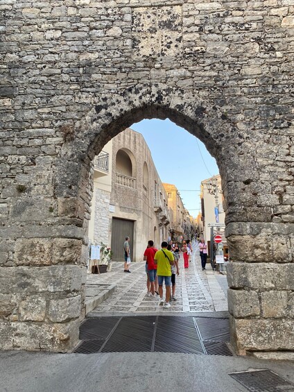An ancient stone archway leading into a narrow street lined with buildings. 4