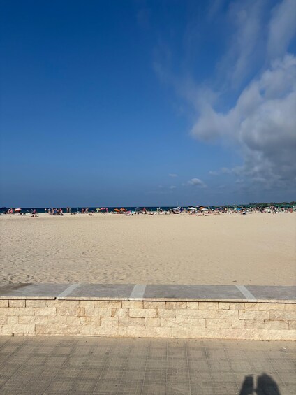 A wide sandy beach with a clear blue sky and a stone wall in the foreground. 5