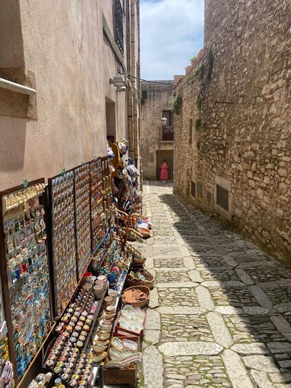 A narrow cobblestone street with a shop displaying ceramic items and a person in traditional attire in the background. 3