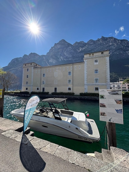 A boat docked at a marina with a mountain backdrop and a large building with a tower. 1