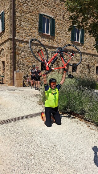 A person holding a bicycle in front of a stone building with green shutters. 1