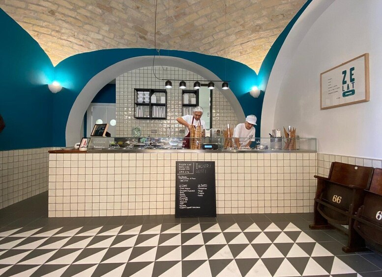 A cafe interior with a checkered floor, a counter with a menu, and a blue arched ceiling. 2