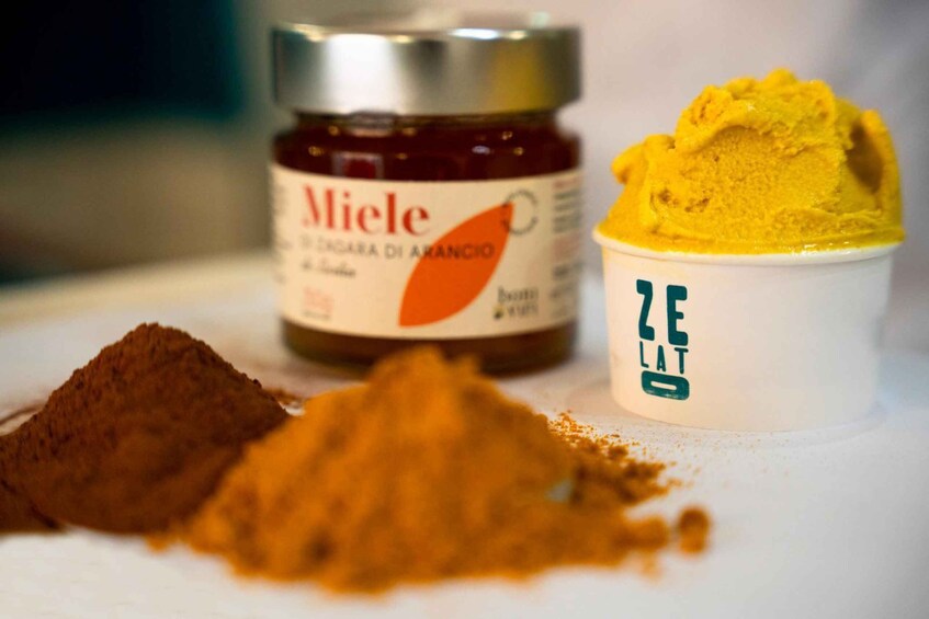 A jar of Miele, a container of yellow ice cream, and a pile of brown powder on a white surface. 4