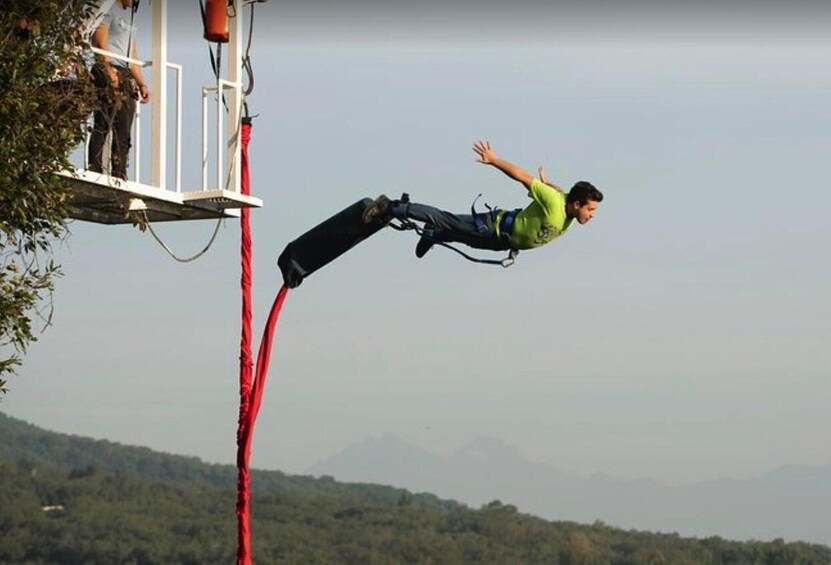A person bungee jumping with a harness and safety gear, a red bungee cord, and a mountainous landscape in the background. 1