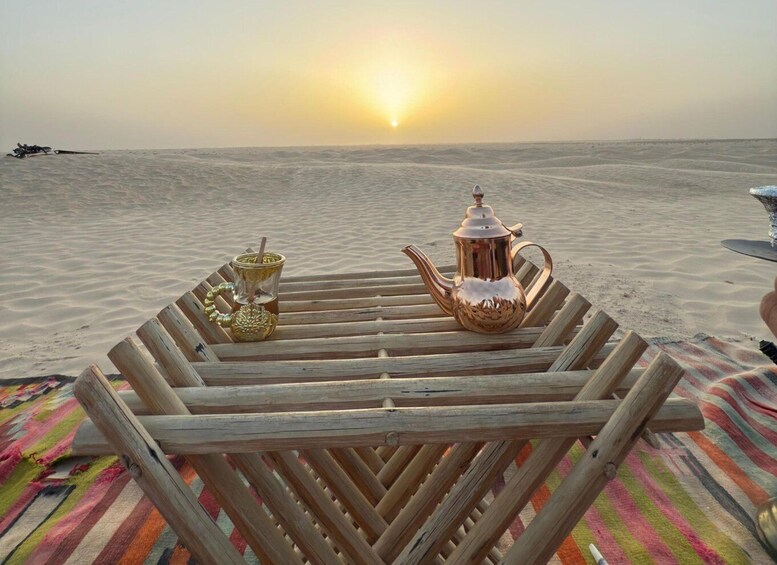 A wooden table with a teapot and a cup on a beach at sunset. 1