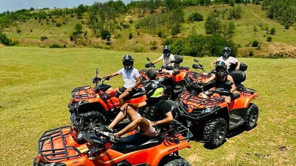 Four people on ATVs in a grassy field with hills in the background. 3