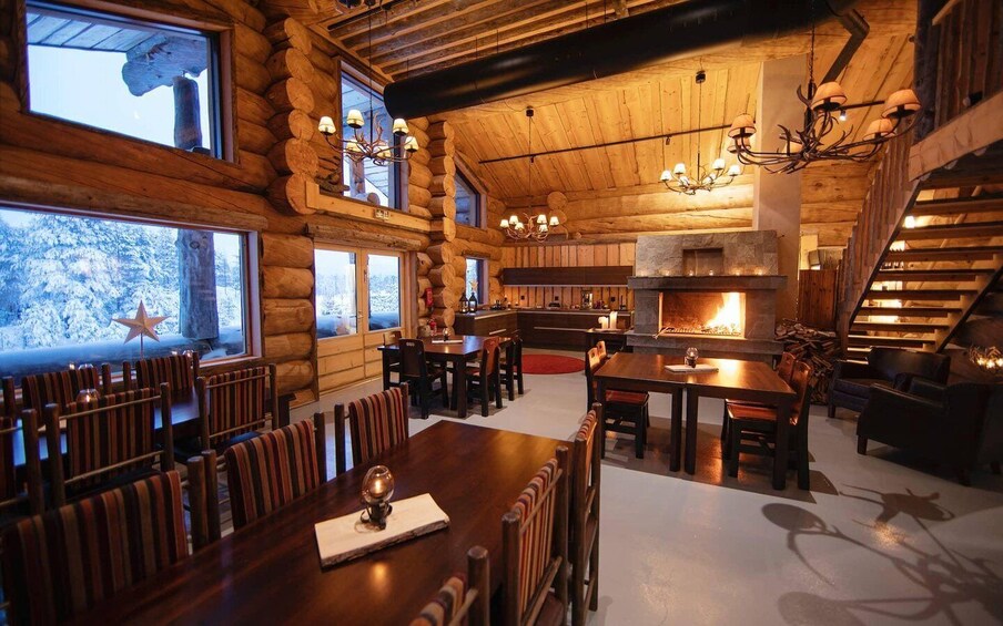 A cozy log cabin interior with a dining area, fireplace, and wooden staircase. 2