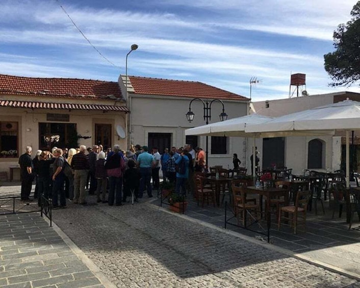 A cobblestone street with a group of people gathered, outdoor seating, and buildings with red-tiled roofs. 2