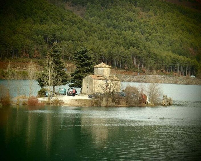 A lakeside church with a stone tower, surrounded by trees and a forested hill. 1