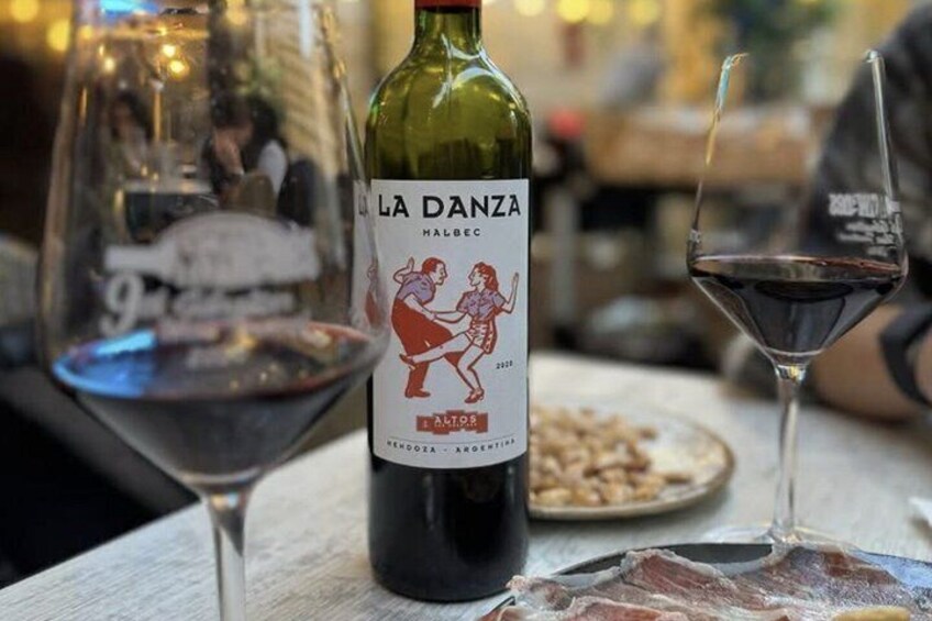 A bottle of La Danza wine, a plate of food, and two wine glasses on a table. 1