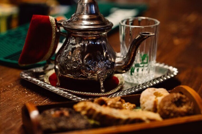 A traditional metal teapot with intricate designs, a glass teacup, and a tray with pastries. 4
