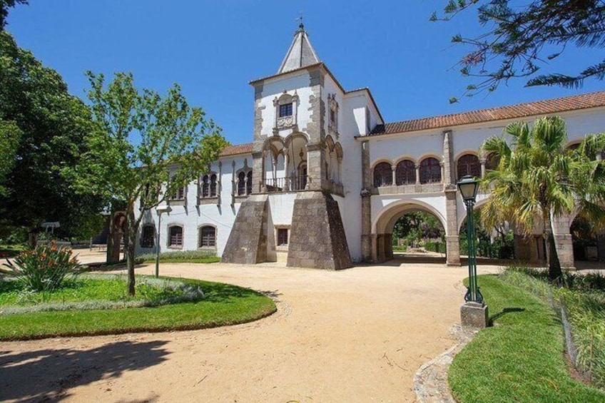 A white colonial-style building with a central tower, surrounded by a landscaped garden with palm trees and a clear blue sky. 1
