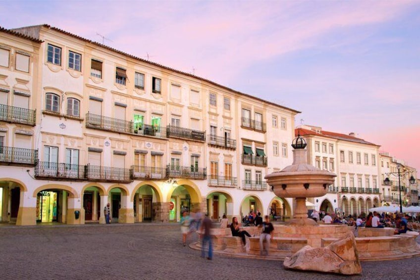 A historic square with a fountain, buildings with balconies, and pedestrians. 2