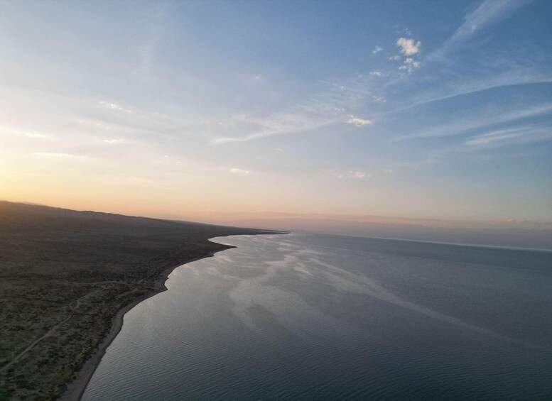 A coastal landscape with a wide expanse of water, a narrow strip of land on the left, and a clear sky. 5
