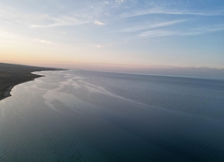 A coastal landscape with a wide expanse of calm sea meeting a sandy shore, under a clear sky. 4