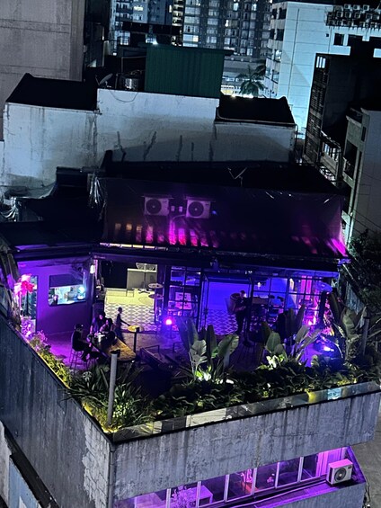 A rooftop bar with purple lighting and outdoor seating surrounded by plants. 1