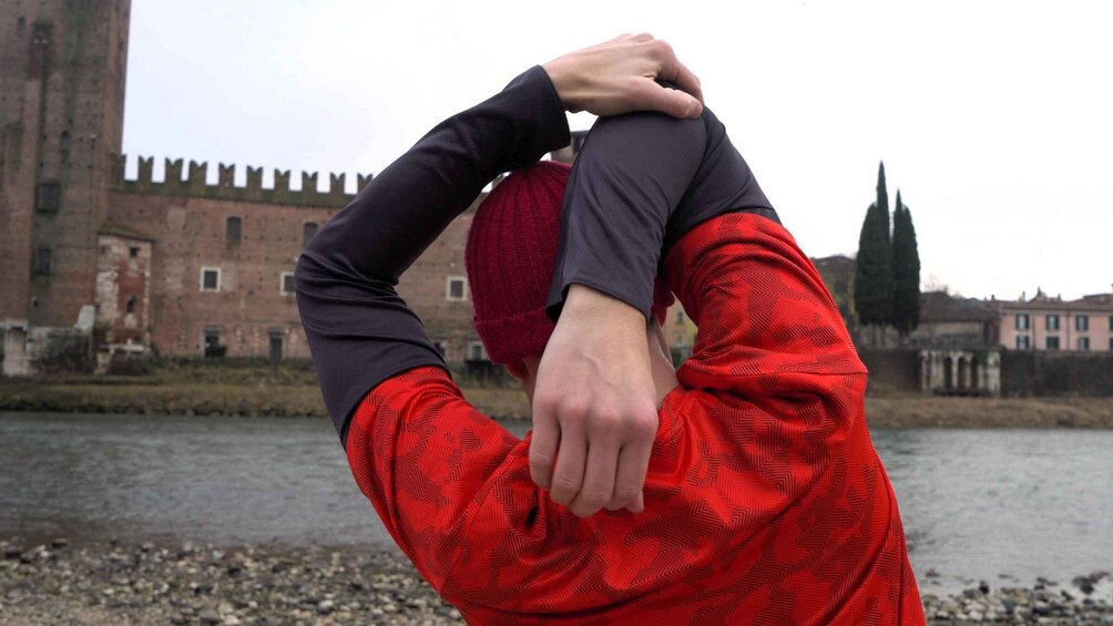 A person stretching by a river with a historic building and a tall tower in the background. 5